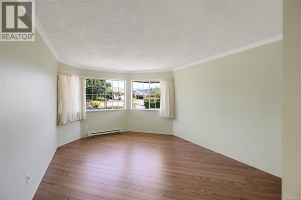Empty room with pale green walls, light wood laminate flooring, and bay windows. - 574 Cedar Cres, Cobble Hill