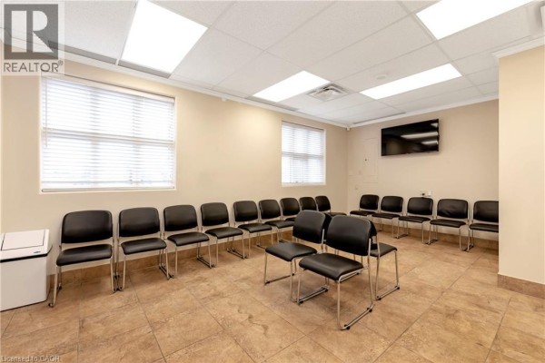 Another view of the waiting area with rows of black chairs and a wall-mounted TV. - 574 Upper James Street, Hamilton