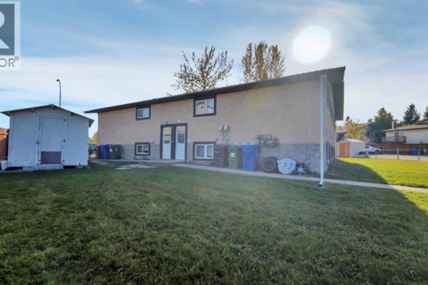Rear view of a stucco duplex with a detached shed and green lawn. - 5743 & 5745 53 Street Close, Rocky Mountain House