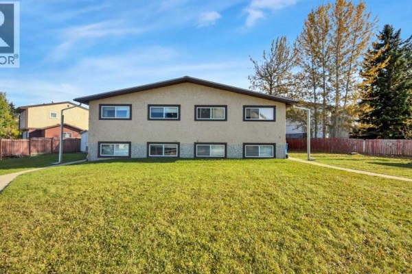Back view of a stucco duplex with multiple windows on two levels and a green lawn. - 5743 & 5745 53 Street Close, Rocky Mountain House