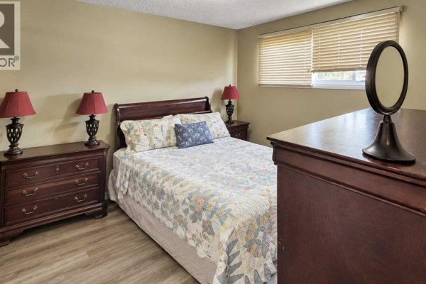 Bedroom with a queen-size bed, two dressers, and blinds on the window. - 5743 & 5745 53 Street Close, Rocky Mountain House