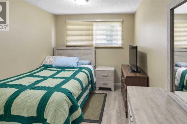 Bedroom with a twin bed, nightstand, dresser, television, and blinds on the window. - 5743 & 5745 53 Street Close, Rocky Mountain House