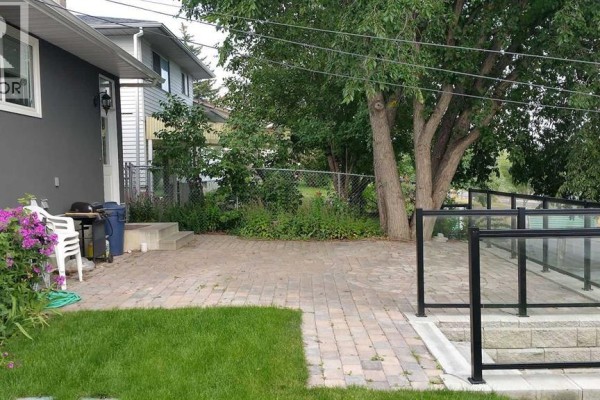 View of a backyard with a paved patio, green lawn, and flowering plants. - 5748 Dalmead Crescent Nw, Calgary