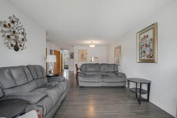 Living room with grey couches, hallway access, and dining area view. - 5749 189 St Nw, Edmonton