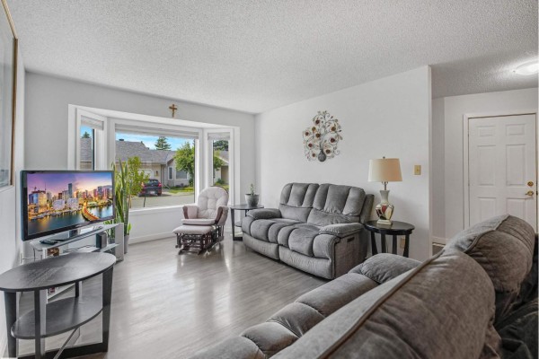 Living room with grey couches, bay window view, and interior door. - 5749 189 St Nw, Edmonton