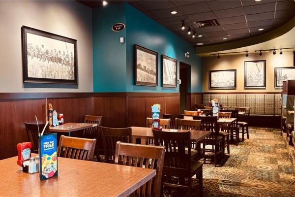 Interior view of the restaurant seating area with wood tables, chairs, and framed artwork on teal walls. - 5753 Hwy 9 Highway, St Andrews