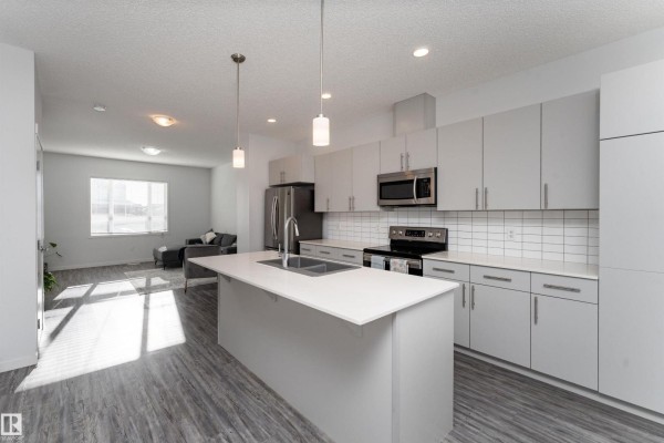 Modern kitchen with light gray cabinets, white subway tile backsplash, and island with sink. - 577 Ebbers Wy Nw, Edmonton