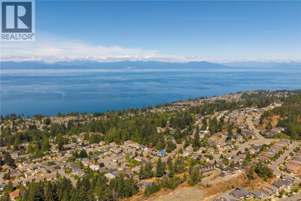 Aerial view of a residential neighborhood with houses nestled among trees, overlooking a vast blue ocean. - 5771 Malibu Terr, Nanaimo