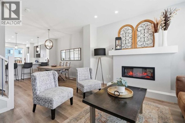 Living room with a fireplace, two armchairs, and view into the dining area with a table and chairs. - 578 Masters Road Se, Calgary
