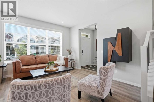 Living room with a sofa, armchairs, a fireplace, and view of the entrance hallway with a textured wall art. - 578 Masters Road Se, Calgary