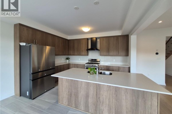 Spacious modern kitchen with large island, stainless steel refrigerator, and warm wood cabinetry. - 578 Telfer Street, Woodstock