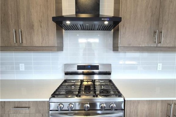 Stainless steel gas range with a black hood vent against a light grey tile backsplash in kitchen. - 578 Telfer Street, Woodstock