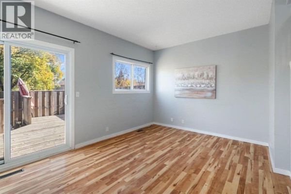 Bedroom with light blue walls, wood floors, and a sliding glass door to a wooden deck. - 58, 5520 1 Avenue Se, Calgary