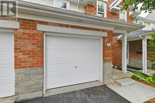 A white garage door on a townhouse featuring red brick and stone base detailing, with a paved driveway. - 58 - 1055 Gordon Street, Guelph