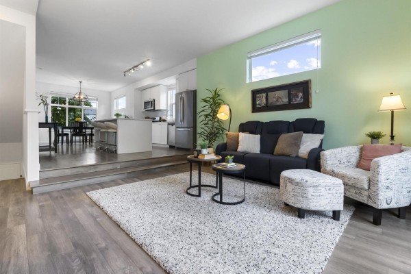 Living room with a mint green accent wall, dark grey sofa, and view into the kitchen. - 58 16678 25 Avenue, Surrey