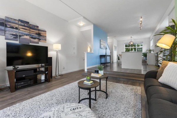 Living room with a large TV, fireplace, grey sofa, and view of the open-concept kitchen. - 58 16678 25 Avenue, Surrey