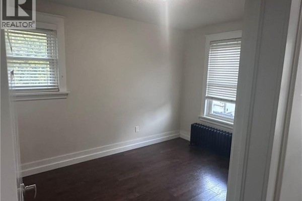 Bedroom with dark hardwood floors, white walls, and two windows with white blinds. - 58-60 Madison Avenue N Unit# 203, Kitchener