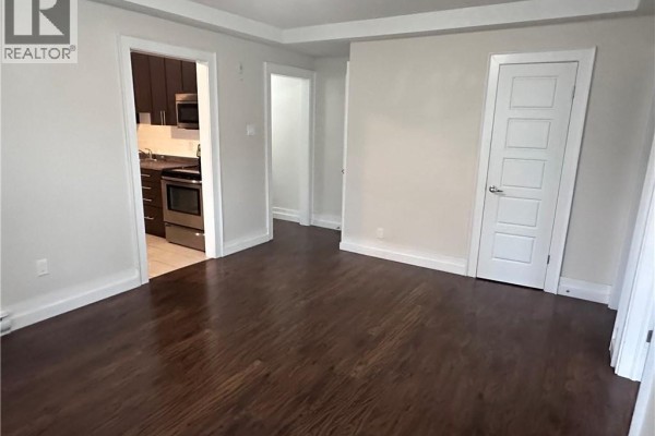 View of the living room, kitchen entrance, and hallway with dark hardwood floors. - 58-60 Madison Avenue N Unit# 203, Kitchener