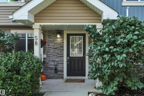 Close-up of the townhouse entrance with a dark door, stone veneer, and landscaping. - #58 9535 217 St Nw, Edmonton