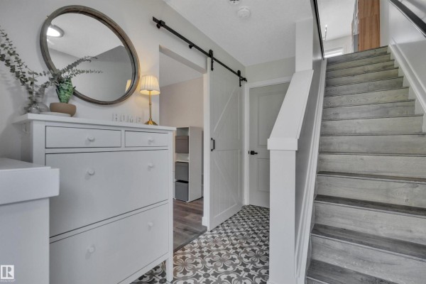 Interior entryway with a white dresser, round mirror, barn door, and stairs. - #58 9535 217 St Nw, Edmonton
