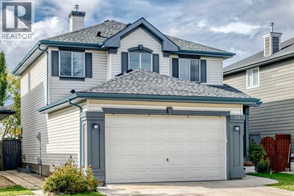 Front view of a two-story beige house with a white garage door and grey roof. - 58 Chaparral Terrace Se, Calgary