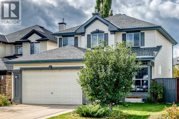 The front of a residential house with a garage, beige siding, and green landscaping. - 58 Chaparral Terrace Se, Calgary