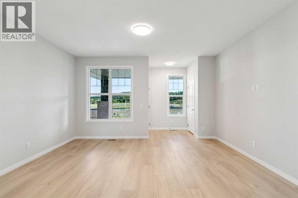 Bright, open-concept living space with light grey walls and light wood flooring. - 58 Creekview Avenue, Calgary