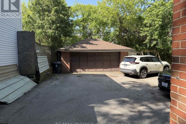 View of a detached brick garage with a brown door and two parked cars. - 58 Forty-first Street, Toronto