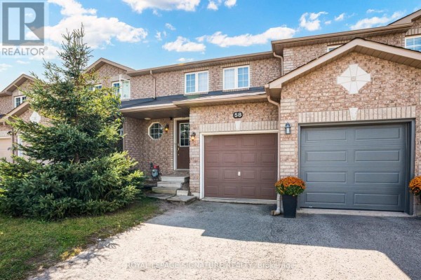 Front entrance of a townhouse with a garage, beige brick exterior and mature evergreen tree. - 58 Goodwin Drive, Barrie