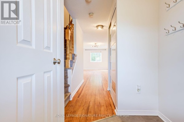 View down a townhouse hallway with white doors, carpeted stairs and hardwood floors. - 58 Goodwin Drive, Barrie