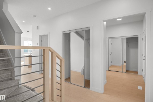 Hallway leading from the entrance with light wood floors, white walls, and mirrored closet doors on the right. - 58 Lemon Cl, Spruce Grove