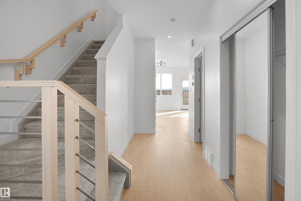 View down a wide, bright hallway showing the staircase and entrances to other rooms, with light wood flooring. - 58 Lemon Cl, Spruce Grove