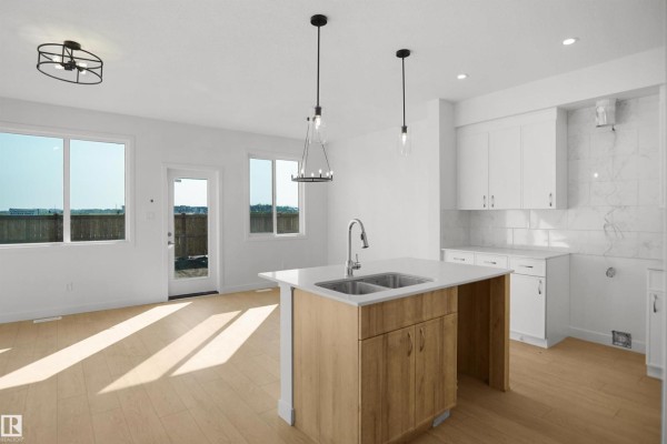 Open concept kitchen and living area with light wood floors, white cabinets, quartz countertops, and large windows. - 58 Lemon Cl, Spruce Grove