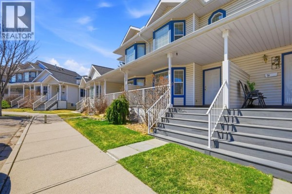 Street view of beige townhouses with white railings and dark grey stairs. - 58 Martin Crossing Court Ne, Calgary