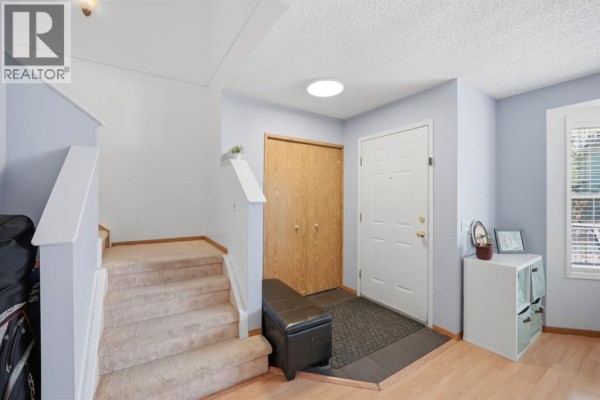 Townhouse entryway with a white door, wood closet doors, and carpeted stairs. - 58 Martin Crossing Court Ne, Calgary