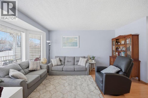 Living room with grey sofas, a dark leather recliner, and a bay window. - 58 Martin Crossing Court Ne, Calgary