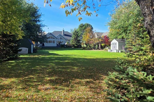 Expansive backyard with a large green lawn, mature trees, and two detached sheds, one green and one white. - 58 Royal Road, Gimli