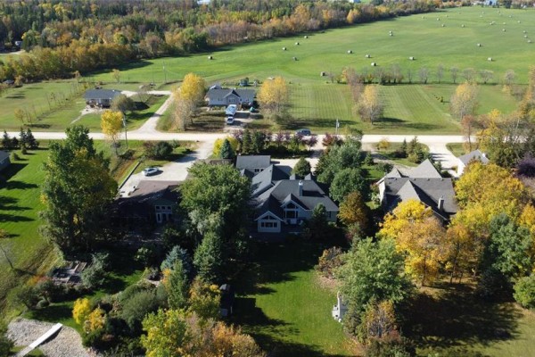 Aerial view of a neighborhood with houses nestled among trees, green fields, and a winding road in the background. - 58 Royal Road, Gimli