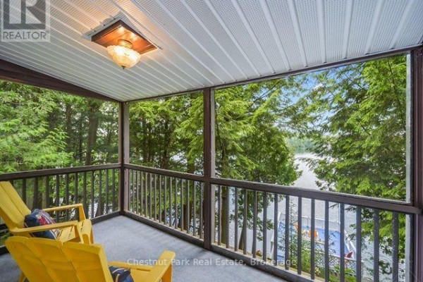 View from trees to a blue deck and dock on a lake with a Canadian flag. - 58 Skyline Drive, Armour