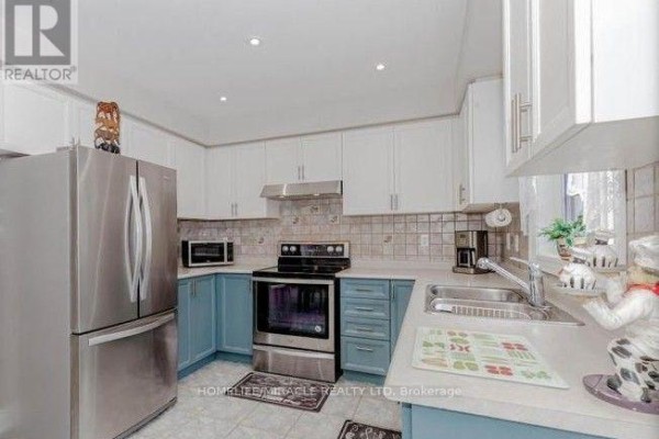 Kitchen with stainless steel refrigerator, stove, white and blue cabinets, and granite countertops. - 58 Summerdale Crescent, Brampton