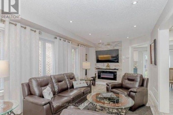 Living room with brown leather sofas, coffee table, electric fireplace, and stone accent wall. - 58 Summerdale Crescent, Brampton