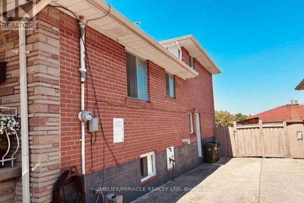 Side exterior of a red brick house showing windows and a wooden fence. - 58 Telco Crescent, Toronto