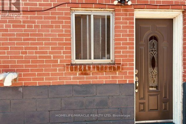 Close-up of a red brick wall with a brown door and a small window. - 58 Telco Crescent, Toronto