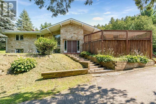 Front view of a stone house with a V-shaped roof, double wooden doors, and tiered wooden garden beds. - 5809 10th Side Road, Essa