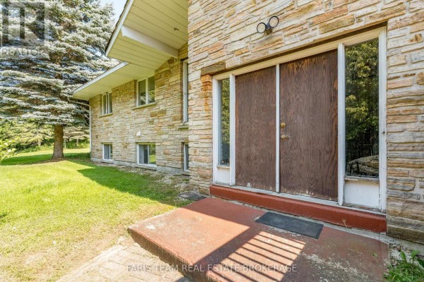 Close-up of a front entrance with double wooden doors, stone exterior, and concrete stoop with grass in the foreground. - 5809 10th Side Road, Essa