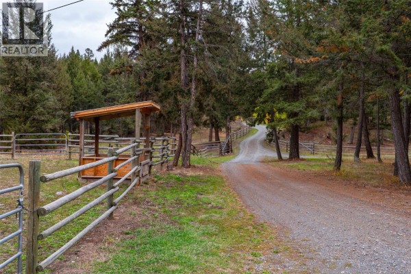 Gravel driveway winding through a treed area with wooden fences and a small covered shelter. - 5809 Beech Road, Merritt