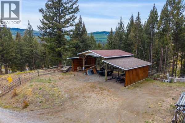 Two wooden carports with metal roofs set in a gravel yard surrounded by trees and fences. - 5809 Beech Road, Merritt