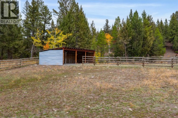 Corrugated metal barn with an open front, surrounded by a wooden fence in a grassy field. - 5809 Beech Road, Merritt