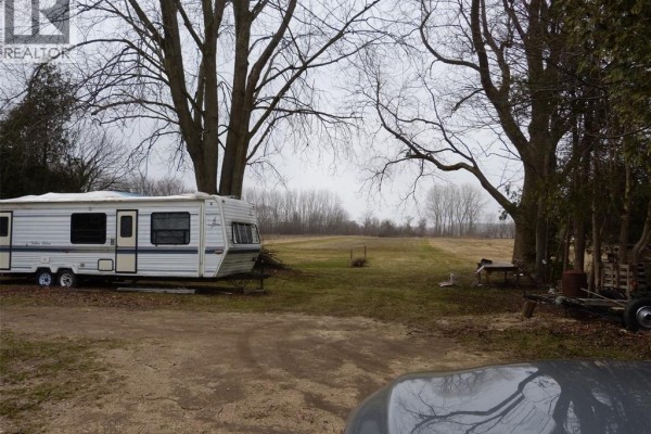 View of open field with parked trailer and trees, overcast sky - 581 Highway 77, Leamington