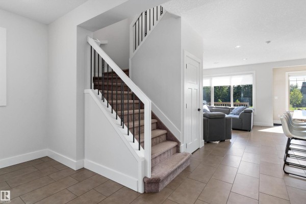 View from foyer towards staircase and living area with large windows and furniture. - 5811 Mullen Pl Nw, Edmonton